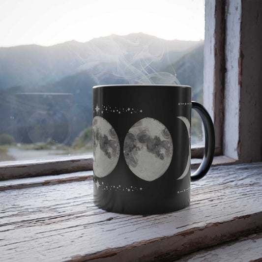 Celestial Color Morphing Mug with moon phases on windowsill, steam rising, mountains in background.