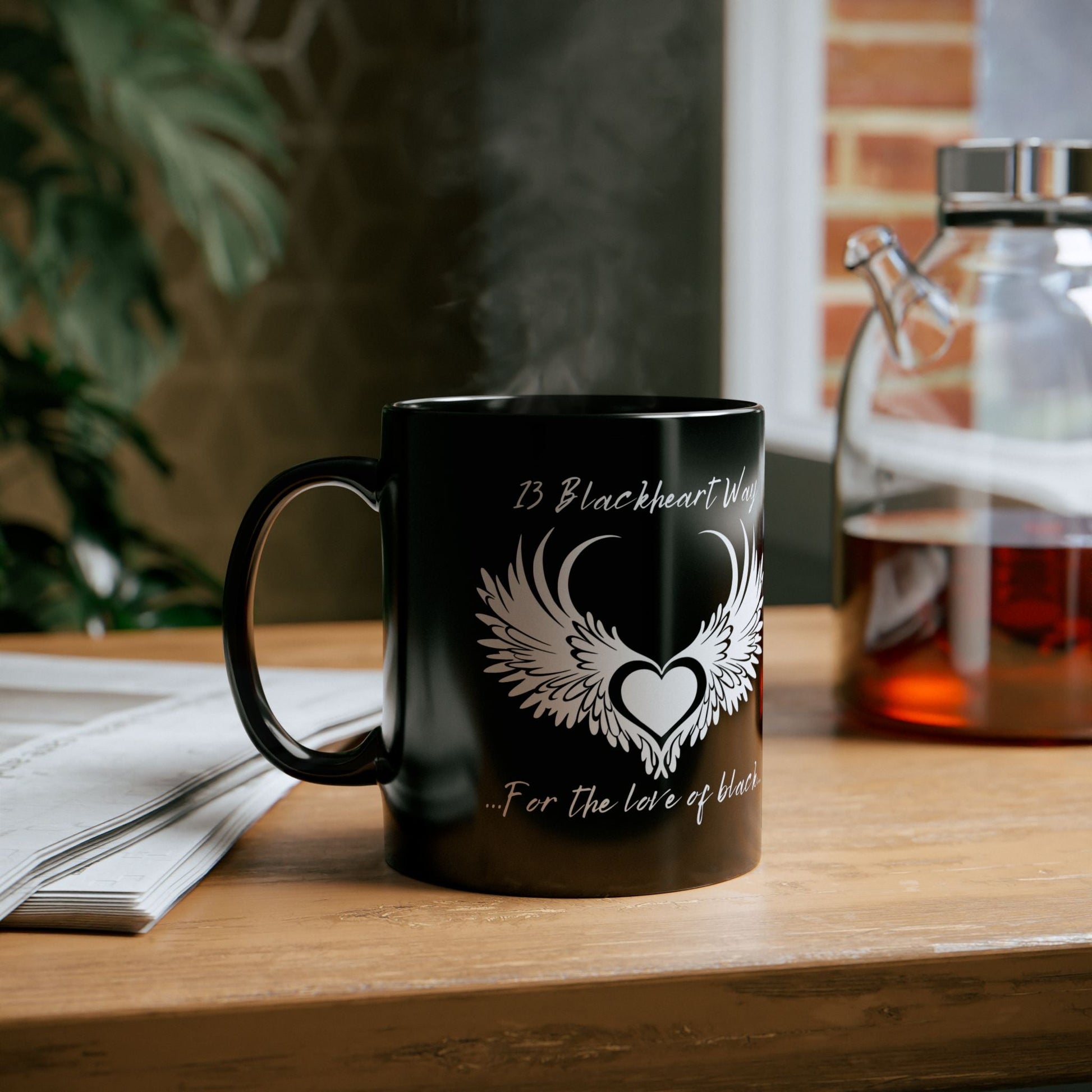 Blackheart Logo Black Mug on a table next to a glass kettle and newspaper.