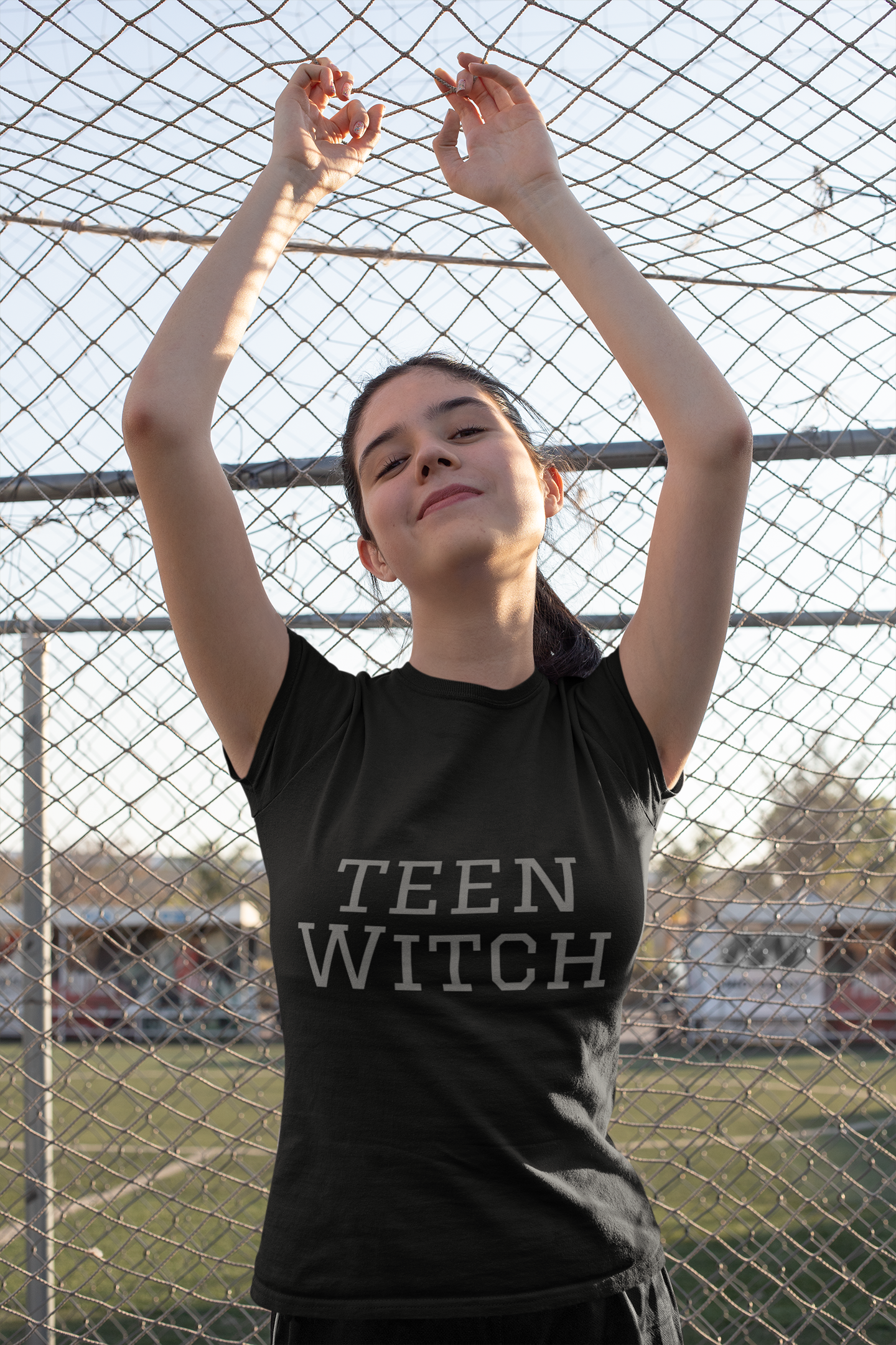 Teen Witch Unisex Jersey Short Sleeve Tee Young woman wearing black unisex short sleeve tee with "Teen Witch" print standing outdoors in front of a chain-link fence