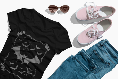 Black Bat Heart Tee with bat graphic print laid flat with sunglasses, pink sneakers, and blue denim jeans on white background