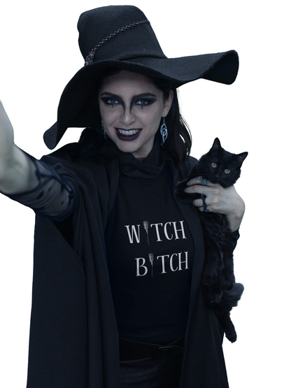 Unisex black jersey short sleeve tee with "W*tch B*tch" text, worn by a person dressed as a witch holding a black cat.