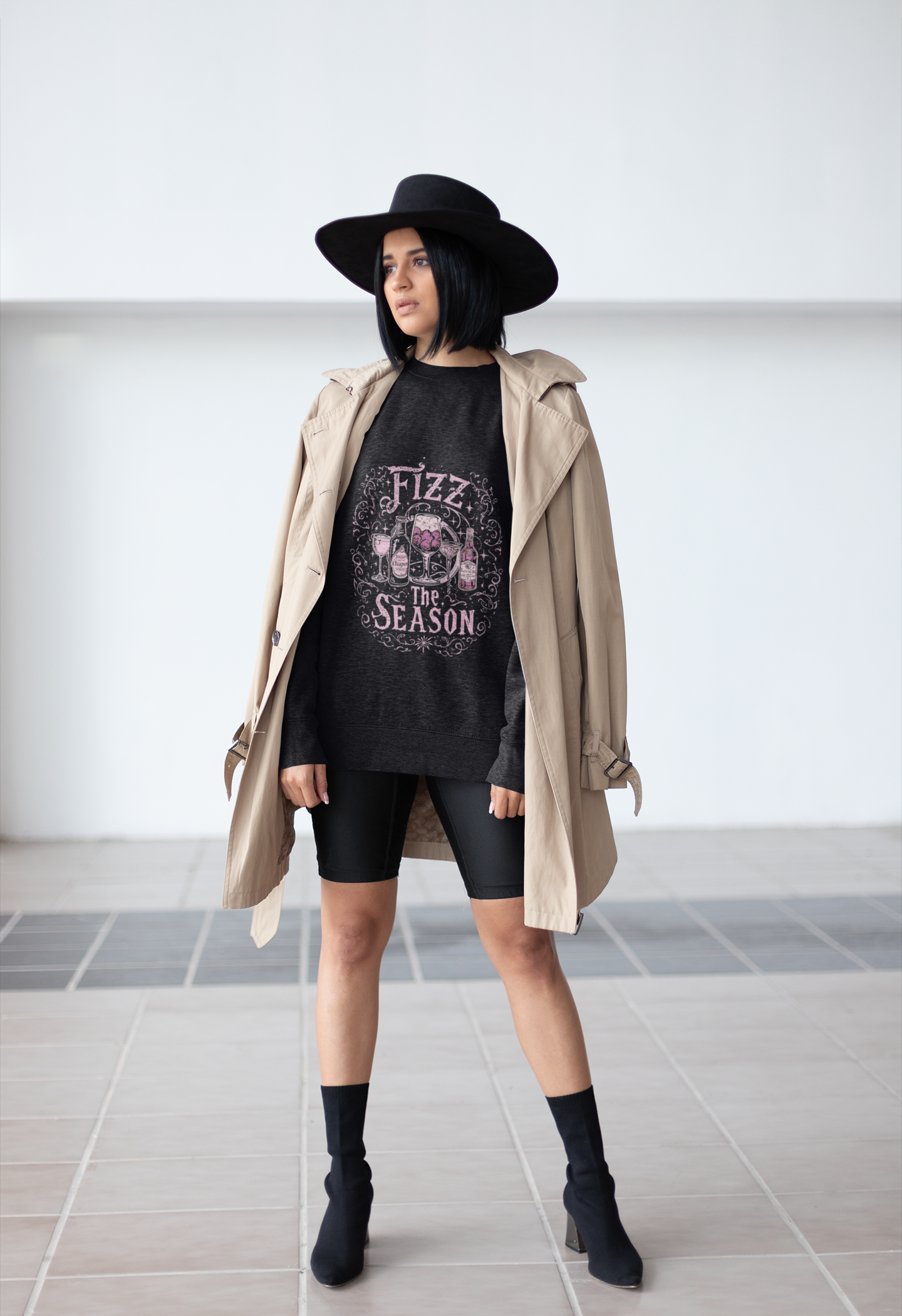 Woman wearing Fizz the Season champagne holiday sweatshirt with trench coat and black hat in an urban setting