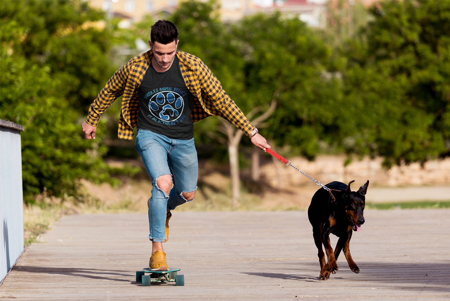 Man skateboarding outdoors wearing Look Good Do Good Tee with dog rescue logo, walking Doberman on leash