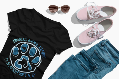 Black "Look Good Do Good" tee with Noodles Animal Refuge paw logo, paired with blue jeans, pink sneakers, and sunglasses flat lay